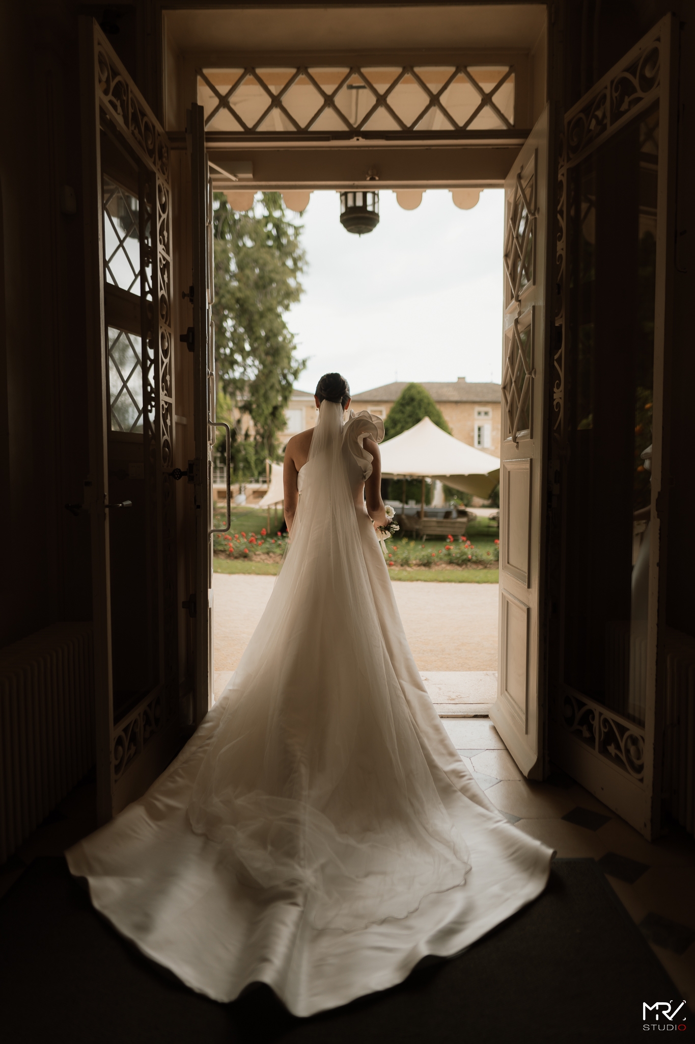 Photographe Mariage à Lyon - MRV Studio Photo | Votre Histoire en Images Mariée de dos en robe à traîne dans l'entrée du Château des Ravatys